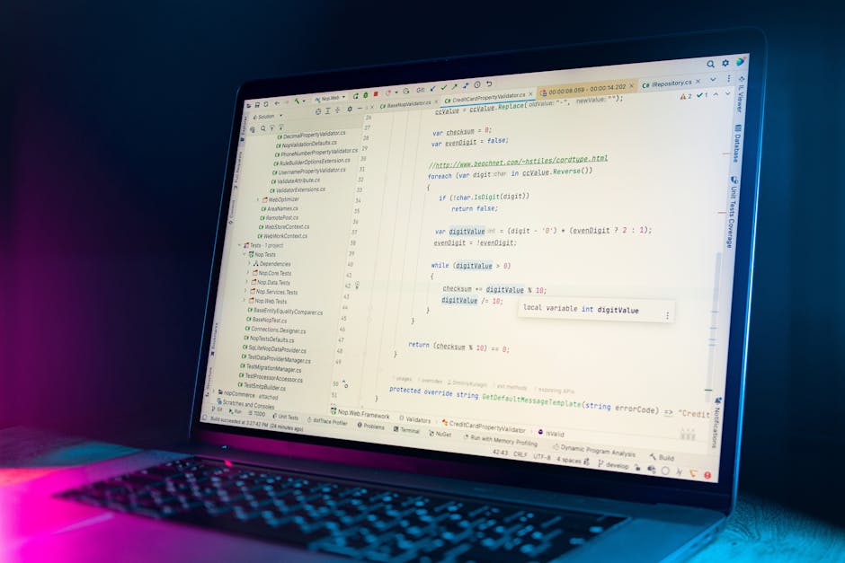 A person with light skin, wearing a white long-sleeve shirt, is typing on a slim black laptop placed on a clean, white surface. The laptop screen displays lines of code and a development interface, wi